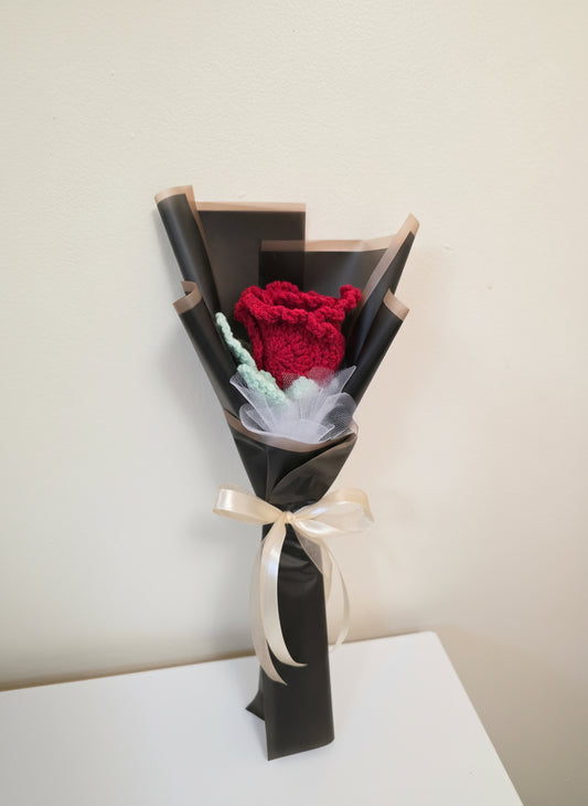 A red rose wrapped in black paper with a white ribbon