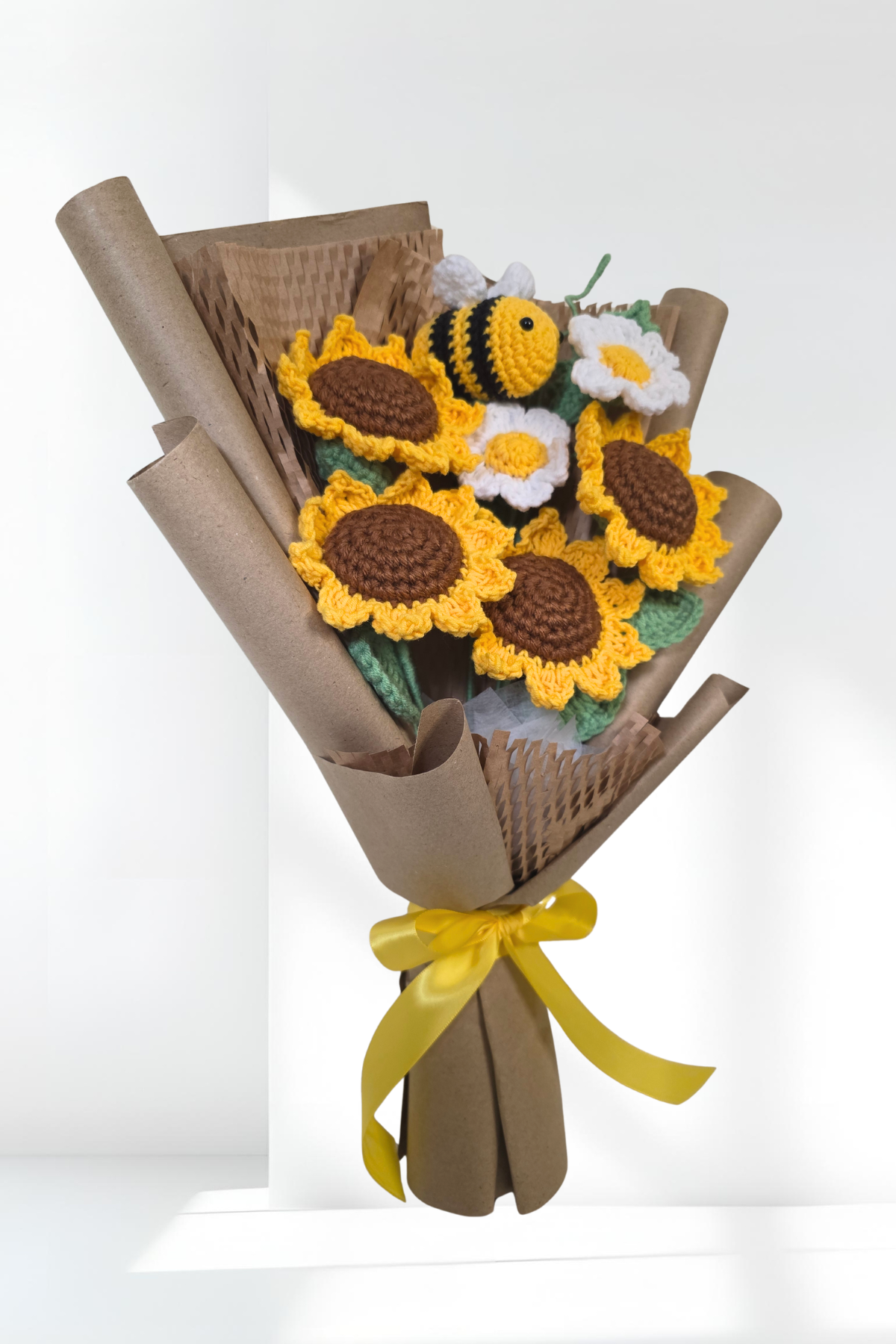Bouquet of crochet sunflowers and bees wrapped in brown paper with a yellow ribbon on a white background.