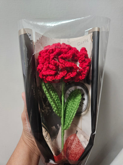 Handcrafted crochet red carnation flower with green leaves, wrapped in black and tied with a satin ribbon for a charming, delicate look.