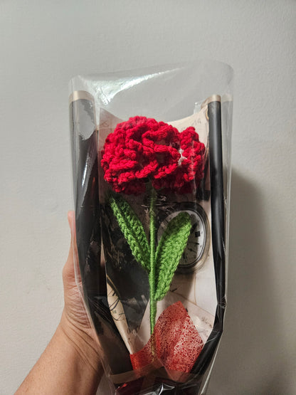 Handcrafted crochet red carnation flower with green leaves, wrapped in black and tied with a satin ribbon for a charming, delicate look.