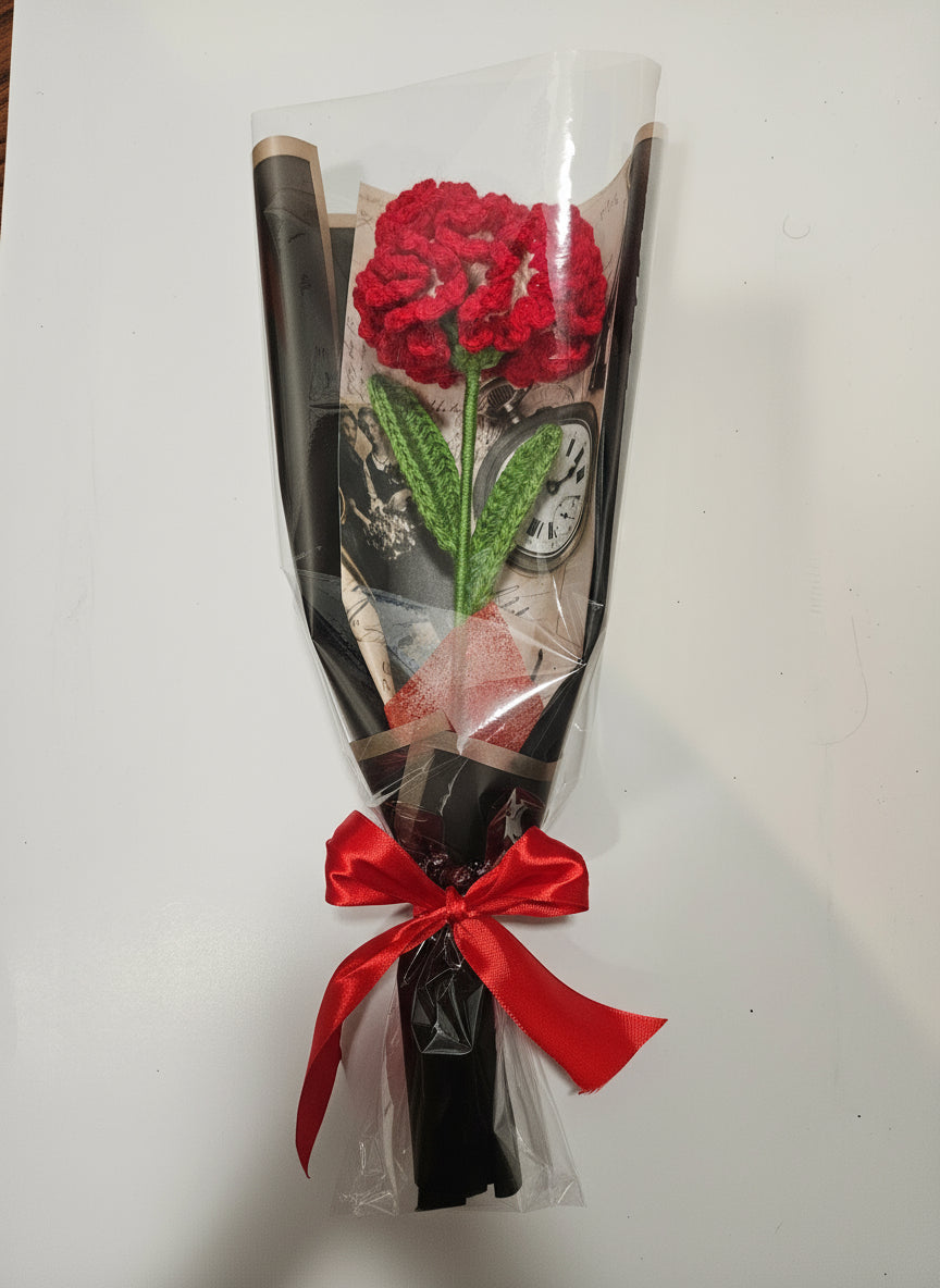 Handcrafted crochet red carnation flower with green leaves, wrapped in black and tied with a satin ribbon for a charming, delicate look.