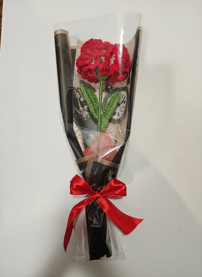 Handcrafted crochet red carnation flower with green leaves, wrapped in black and tied with a satin ribbon for a charming, delicate look.