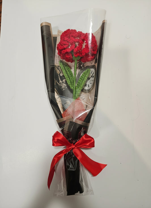Handcrafted crochet red carnation flower with green leaves, wrapped in black and tied with a satin ribbon for a charming, delicate look.