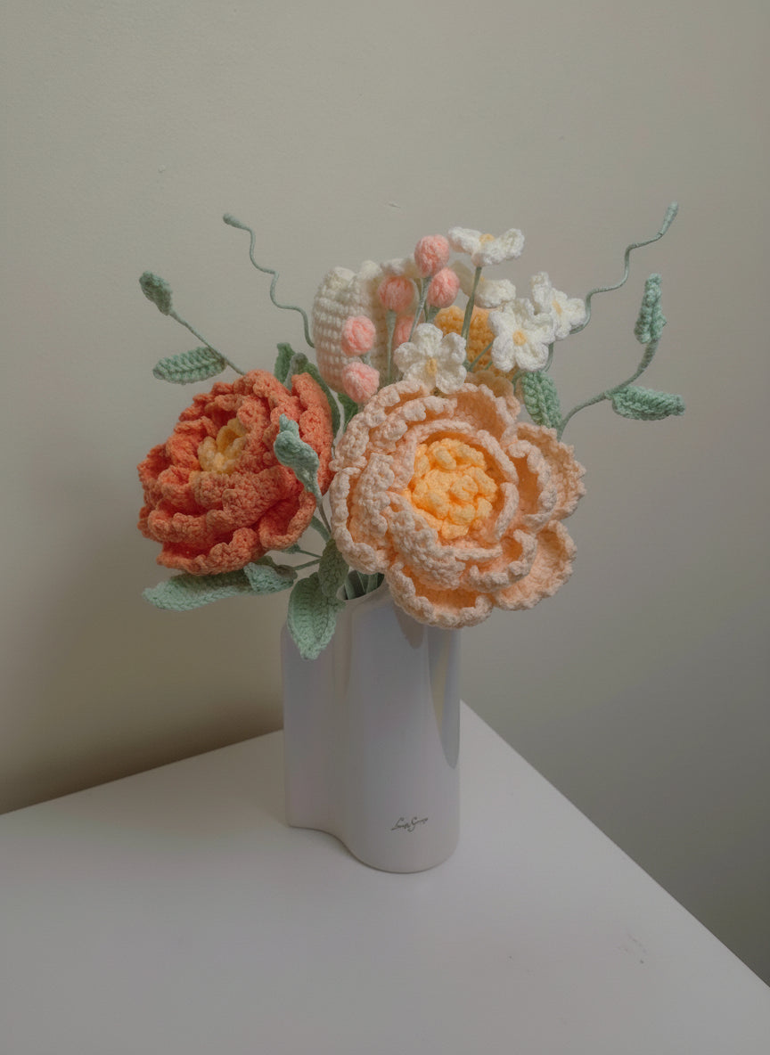 Crocheted peony and tulip bouquet on a white surface with a neutral background