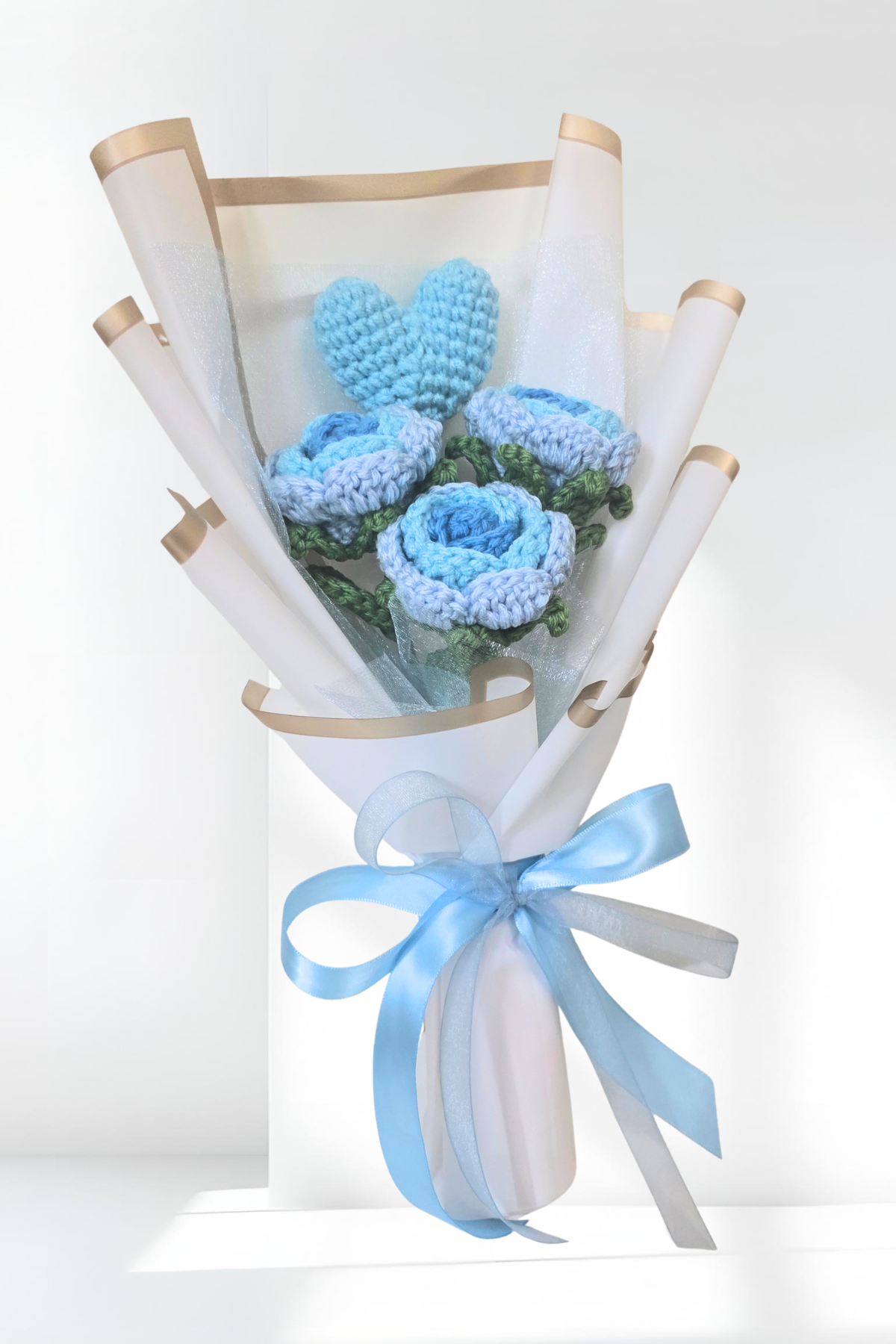 Bouquet of blue crocheted flowers wrapped in white paper with a blue ribbon on a white background