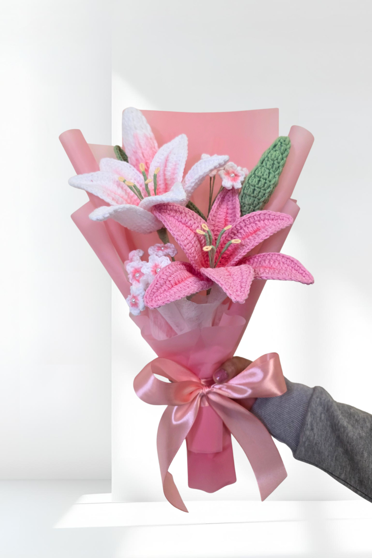 Bouquet of pink lily  flowers with a pink ribbon held by a hand against a white background
