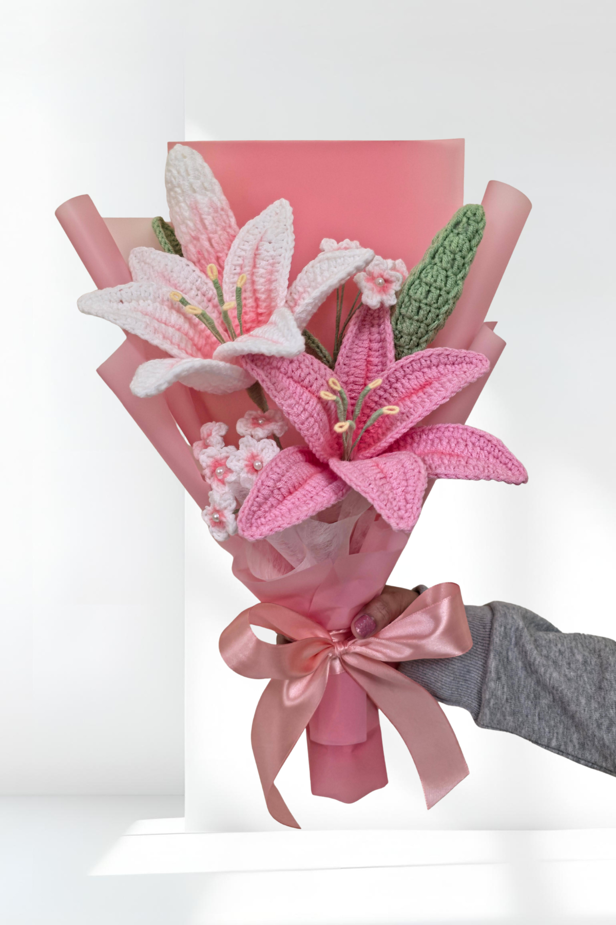 Bouquet of pink and white lily flowers wrapped in pink paper with a hand holding it against a white background