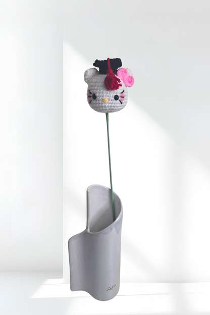 Crocheted Hello Kitty head with a pink flower in a white vase on a white background