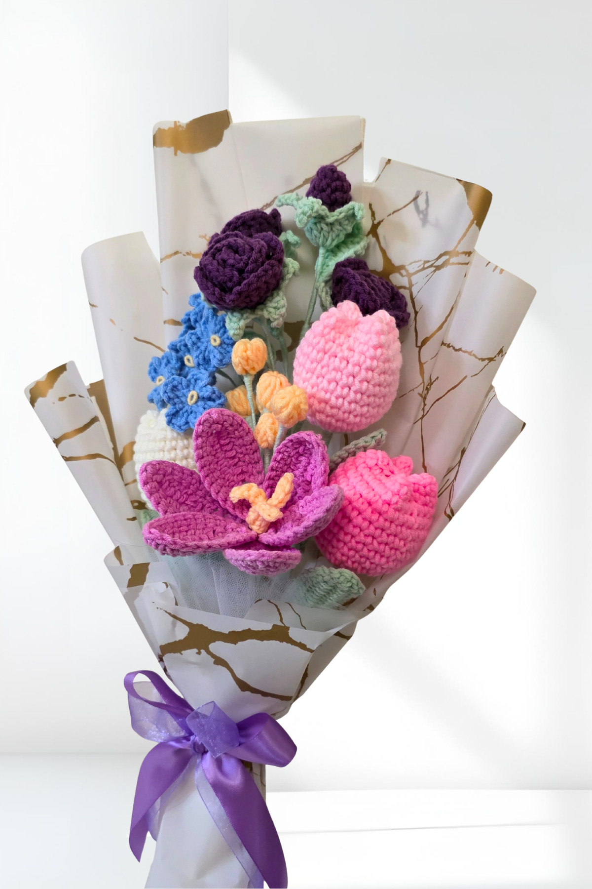 Bouquet of colorful knitted flowers wrapped in paper with a purple ribbon on a white background
