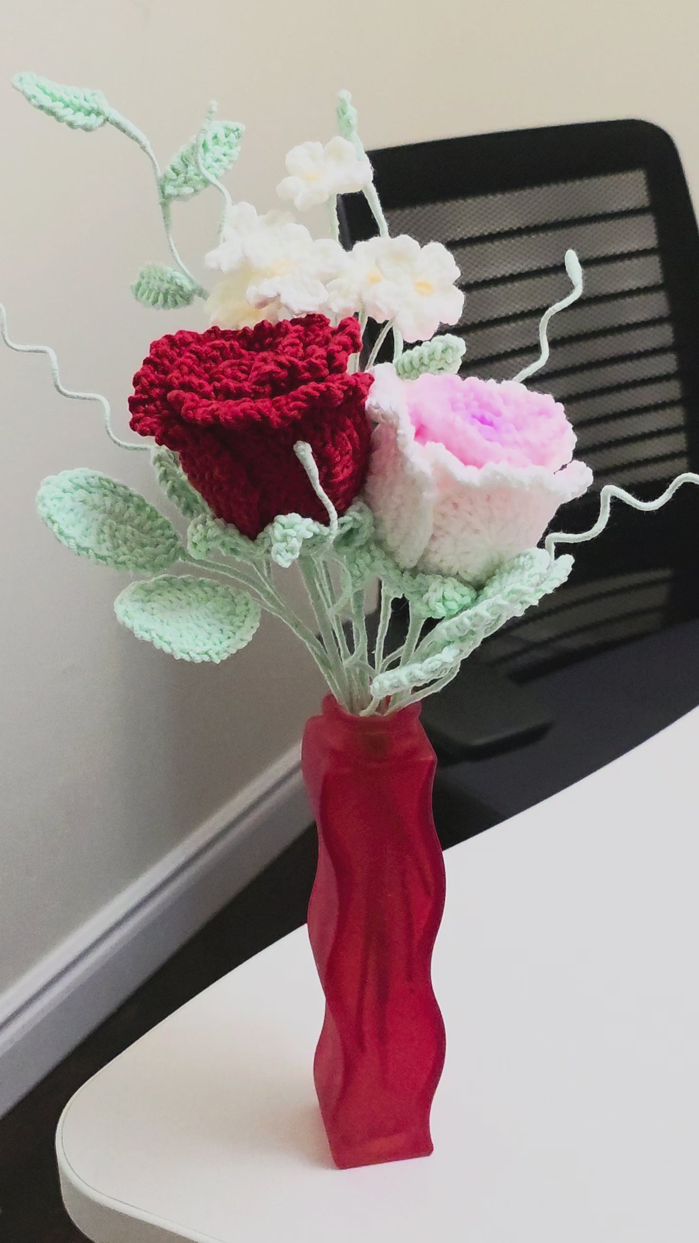 Decorative flower arrangement in a red vase on a white surface with a light gray background