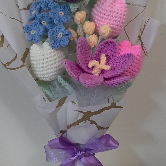 A crochet flower bouquet with charming blend of purple roses, blue blossoms, and soft pastel tulips