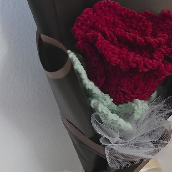 Bouquet of crocheted rose flower wrapped in black paper with a bow on a white background