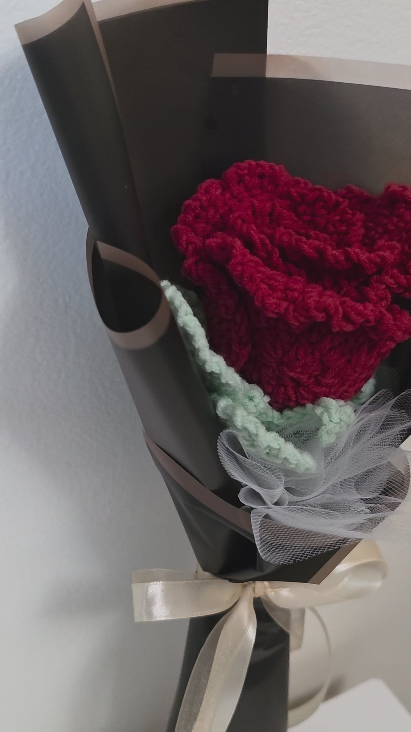 Bouquet of crocheted rose flower wrapped in black paper with a bow on a white background