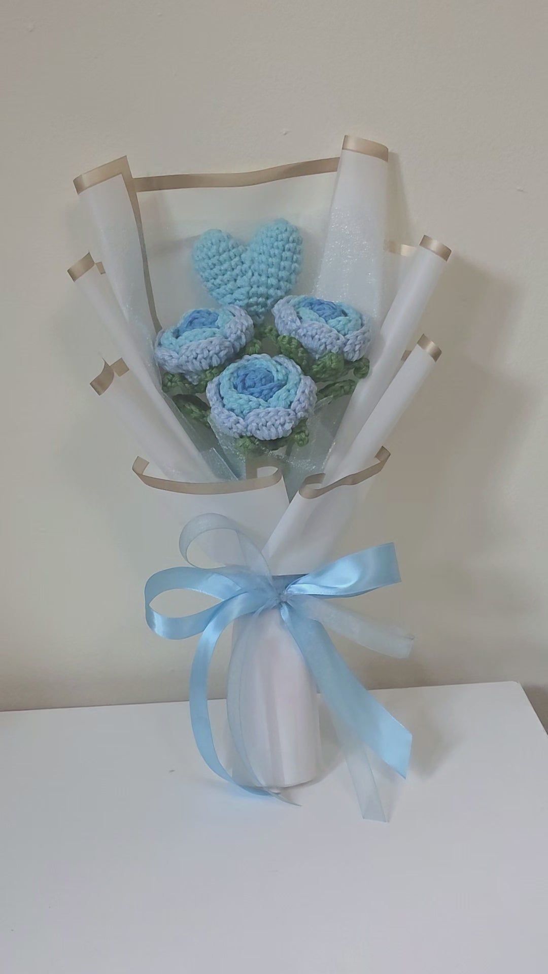 Bouquet of blue crocheted flowers wrapped in white paper with a blue ribbon on a white background
