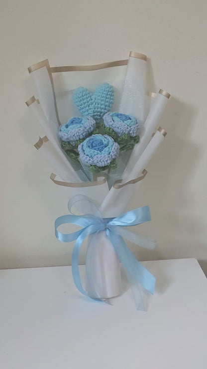 Bouquet of blue crocheted flowers wrapped in white paper with a blue ribbon on a white background