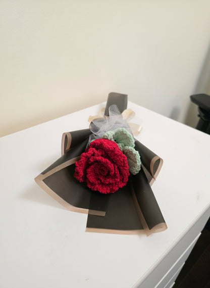 A red rose wrapped in black paper with a white ribbon